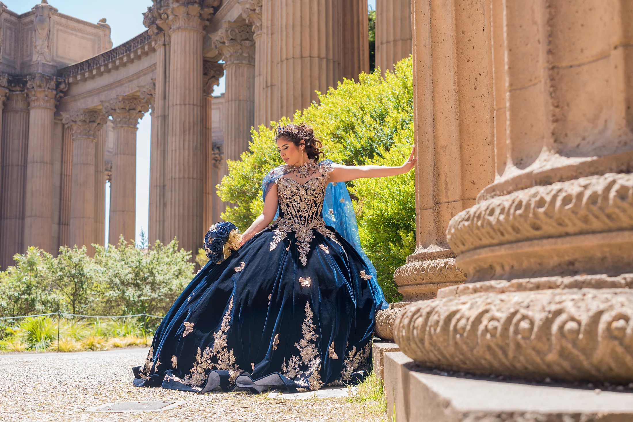 Quinceañera con vestido azul marino posando entre columnas en California