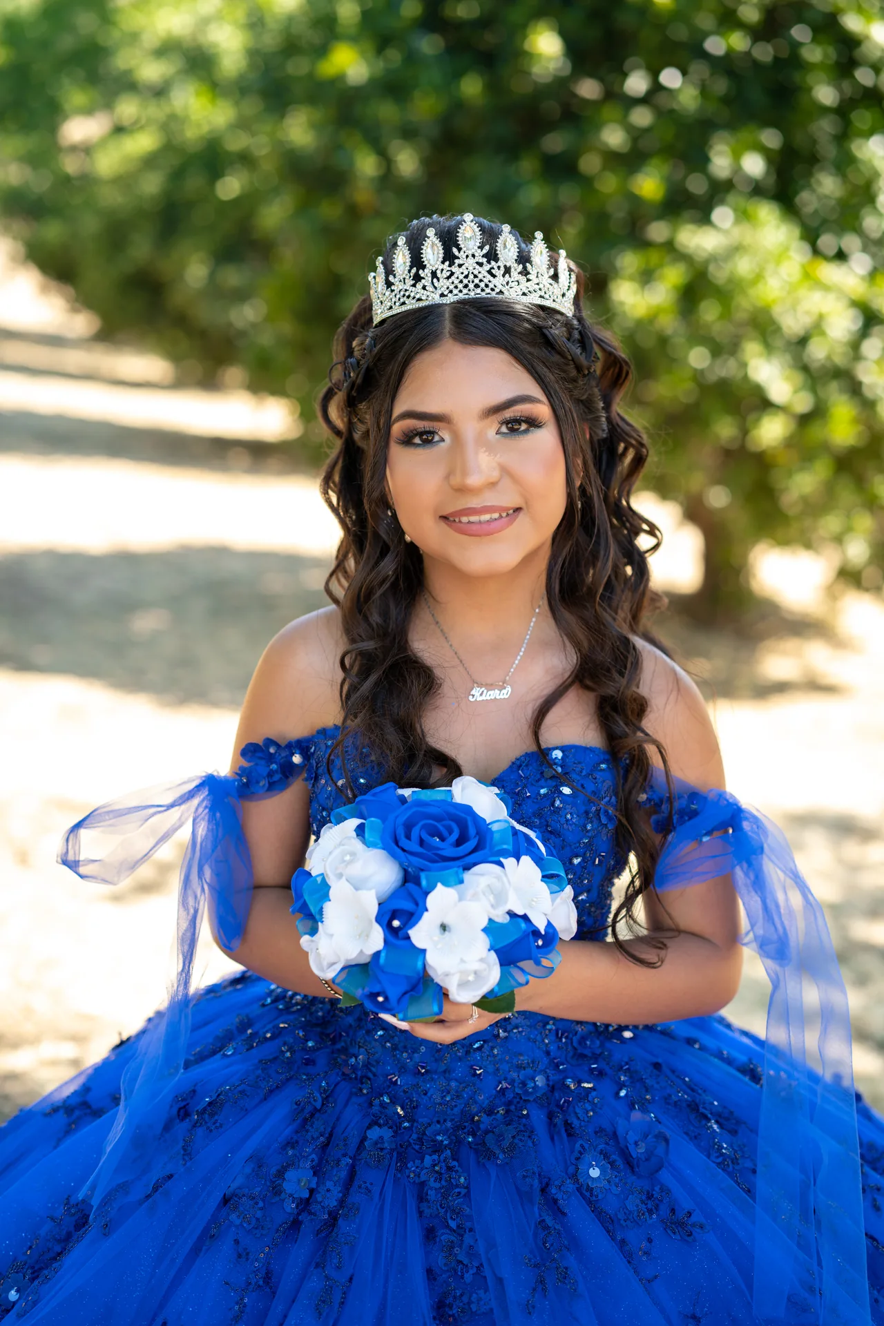 Retrato individual de quinceañera con vestido azul, corona y bouquet
