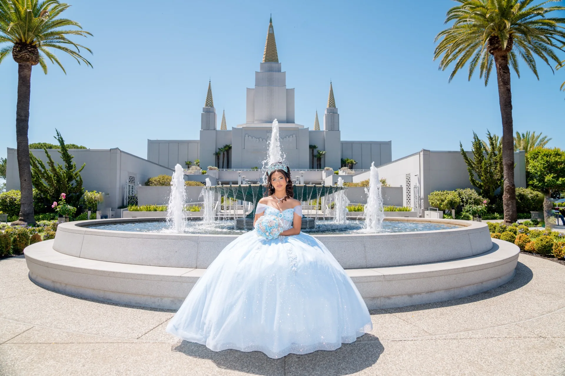 Quinceañera con vestido celeste frente a las fuentes y la arquitectura del Templo de Oakland, California